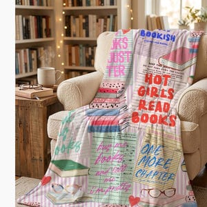 May include: A cozy throw blanket draped over an armchair, featuring a bookish theme. The blanket is covered in book illustrations, text, and phrases like "Hot Girls Read Books" and "One More Chapter." The background includes a bookshelf and a side table with a mug and glasses.