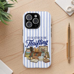 Peut inclure: Coque de téléphone à rayures bleues et blanches. Elle affiche le texte "I'D RATHER BE Thrifting" et des illustrations de livres, d'un poulet et d'autres objets vintage, évoquant le goût pour les trouvailles.