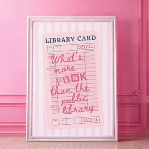 May include: A framed print featuring a pink library card design with the text "What's more PUNK than the public library." The print has a white frame and is set against a pink and white striped background.