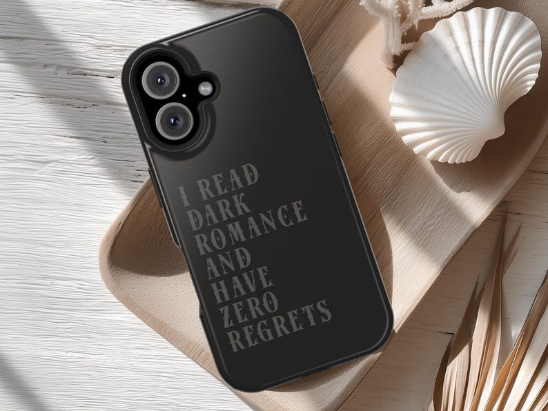 May include: Black phone case with the text "I READ DARK ROMANCE AND HAVE ZERO REGRETS" in a gray font. The phone case is on a wooden tray with a white seashell.