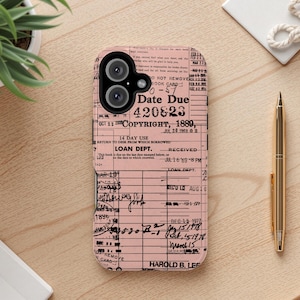 May include: A pink phone case with a vintage library card design, featuring the text "Date Due 420823" and "Copyright, 1889". The case is on a wooden surface with a gold pen and a small plant.