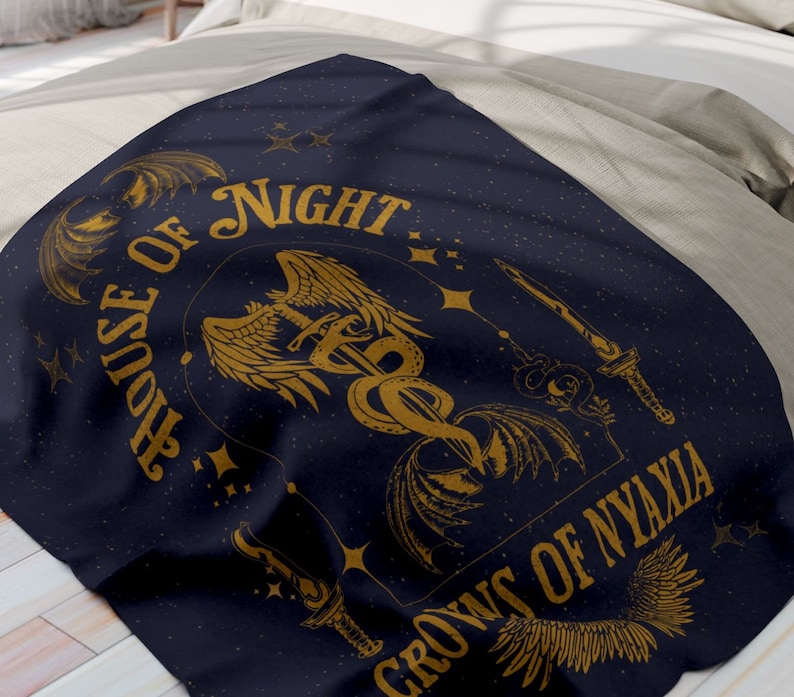 May include: A dark blue throw blanket with a gold design featuring a winged serpent, a sword, and the text "House of Night Crowns of Nyaxia".