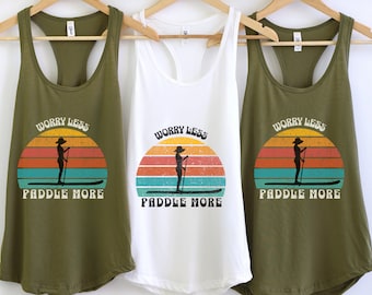 May include: Three tank tops with a retro sunset graphic and the text "Worry Less Paddle More". The tank tops are in olive green and white.