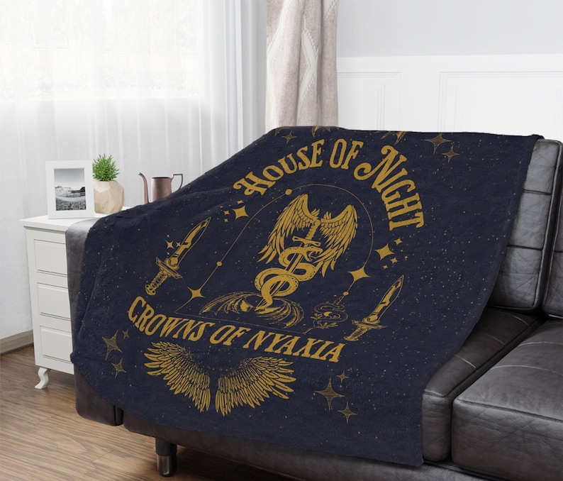 May include: A dark blue throw blanket with a gold design featuring a winged serpent, a dagger, and the text "House of Night Crowns of Nyaxia".