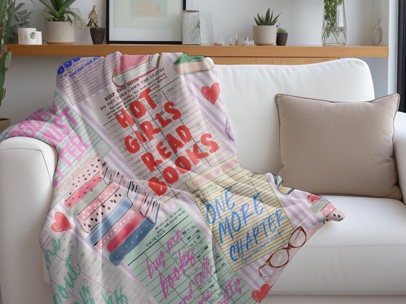 May include: A soft, printed throw blanket draped over a white sofa. The blanket features a collage of book-themed graphics, including the text "HOT GIRLS READ BOOKS" in red, and "ONE MORE CHAPTER" in blue. Pink hearts and book illustrations are also present.