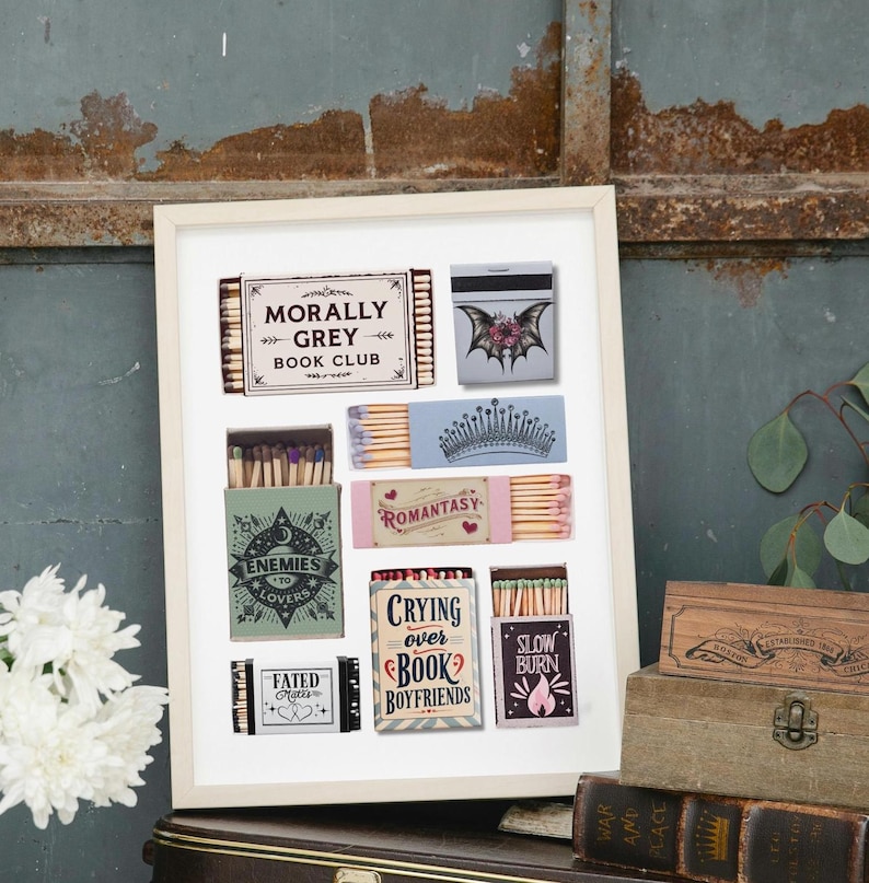 May include: A framed art print featuring various matchbox designs with text. The matchboxes have different themes, including "Morally Grey Book Club," "Enemies to Lovers," and "Crying Over Book Boyfriends." The color palette includes shades of gray, pink, and green.