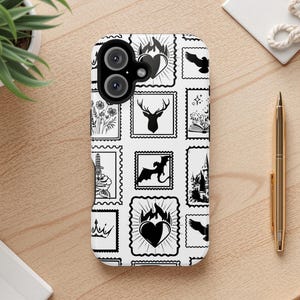 May include: A white phone case featuring a repeating pattern of black postage stamp designs. The stamps depict various illustrations, including a deer head, a dragon, a heart with flames, and a castle. The case is on a wooden surface.