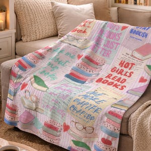 May include: A soft, light pink throw blanket with a collage of book-themed graphics. The blanket features stacks of books, glasses, and text that reads "Hot Girls Read Books" and "Stay Bookish".