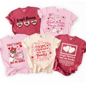 May include: Five t-shirts in various colors, including pink and burgundy, are displayed. Each shirt features a unique graphic design with the phrase "Forget Flowers, Buy Me Books." The designs include hearts, books, and other decorative elements.