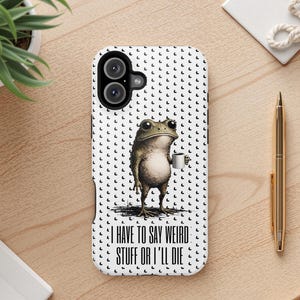 Pode incluir: Uma capa de telefone branca com um desenho animado de um sapo segurando uma xícara de café. O sapo é marrom e verde, em um fundo de pequenas formas de meia-lua pretas. O texto "I HAVE TO SAY WEIRD STUFF OR I'LL DIE" está impresso na capa.