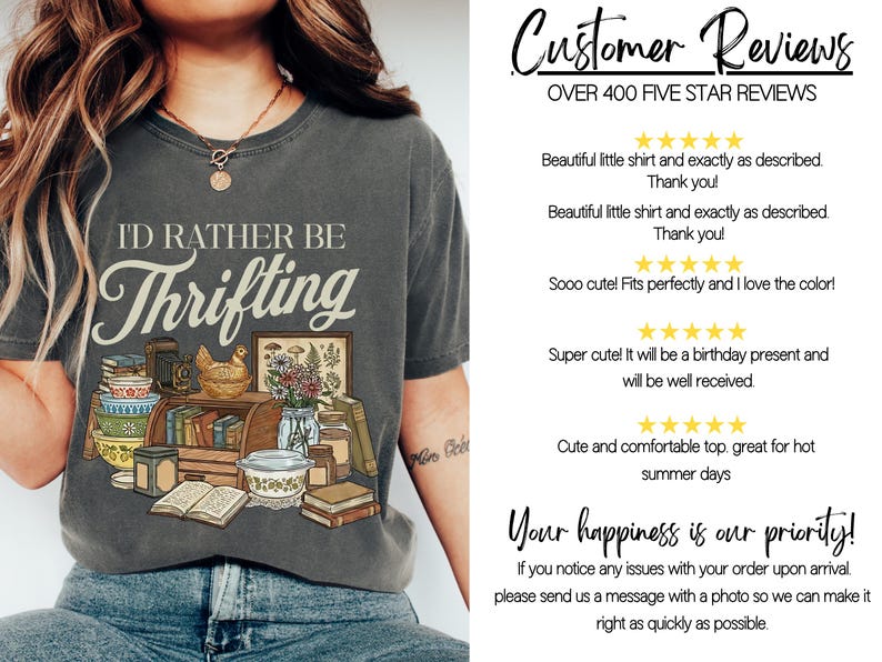 May include: Dark gray t-shirt with the text "I'd Rather Be Thrifting" in a vintage style. The graphic includes books, a camera, a chicken figurine, and a framed botanical print. The shirt is worn by a person.