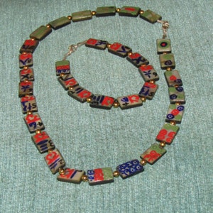 May include: A set of two necklaces made of colourful, rectangular beads with gold accents. The larger necklace is longer and has a more intricate design than the smaller necklace.