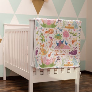 May include: White crib with a colorful animal print blanket hanging on the side. The blanket features a variety of animals, including a lion, a penguin, a kangaroo, and a giraffe. The crib is in a room with a light blue and white geometric wallpaper.