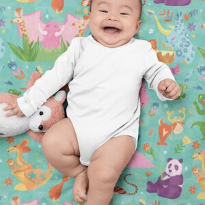 May include: A baby wearing a white long-sleeved onesie is lying on a colorful blanket with a variety of animal illustrations. The blanket features a green background with pink, orange, and blue animal illustrations.
