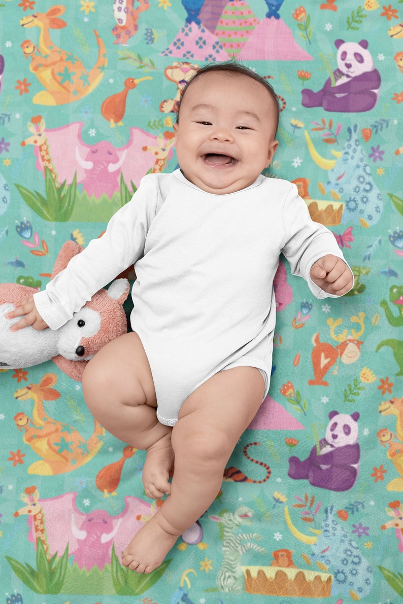 May include: A baby wearing a white long-sleeved onesie is lying on a colorful blanket with a variety of animal illustrations. The blanket features a green background with pink, orange, and blue animal illustrations.