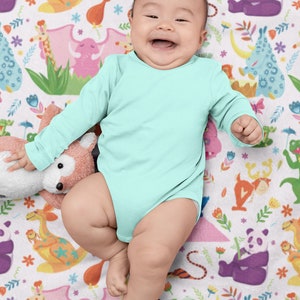 May include: A baby wearing a light blue long-sleeved onesie is lying on a white blanket with a colorful animal print. The baby is smiling and looking at the camera.