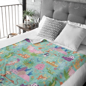 May include: A teal blue fleece blanket with a colorful pattern of animals, including a panda, a tiger, a monkey, and a dragon. The blanket is on a bed with white pillows and a gray headboard.