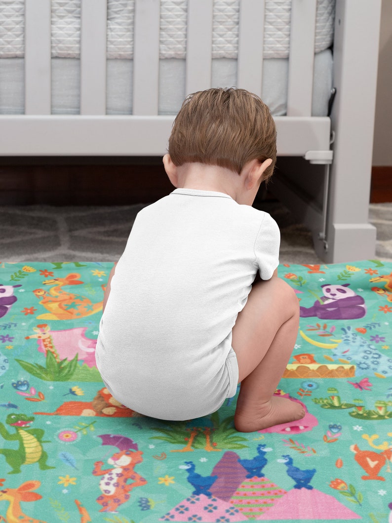 May include: A baby sitting on a colorful play mat with a jungle animal theme. The mat features a variety of animals, including a lion, a giraffe, a panda, and a monkey. The mat is made of soft, plush fabric and is perfect for babies and toddlers.