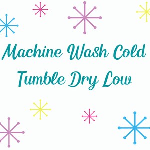 May include: A white background with the text "Machine Wash Cold Tumble Dry Low" in teal blue.  There are nine snowflakes in various colors, including pink, blue, and yellow.