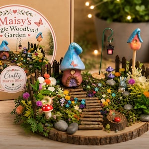 Op de afbeelding: Een miniatuur bostuinset met een centraal paddenstoelvormig huisje met een blauw dak, een houten pad, een klein hekje, een lantaarn op een groene draadstandaard, een vogelhuisje, een konijnenfiguurtje en kunstbloemen op een houten basis.