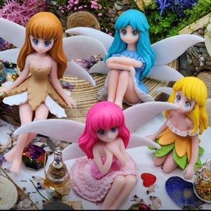 May include: Four fairy figurines with large white wings, each with a different hair color: orange, blue, pink, and yellow. The fairies are in various poses, wearing dresses in matching colors. Decorative bottles and small objects surround them.