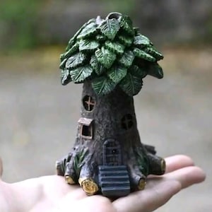 Könnte beinhalten: Eine Miniatur-Baumhausfigur mit einem dunkelbraunen, strukturierten Stamm mit ausgeprägter Wurzelbasis, einer kleinen Treppe, die zu einer Tür führt, zwei runden Fenstern und einer dichten Krone aus geformten grünen Blättern am oberen Teil.