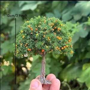 May include: A miniature model tree with a textured brown trunk and a dense green canopy featuring small orange fruit accents. A vertical black line indicates a height of 10 cm, which is equivalent to 3.9 inches, for this scale model.