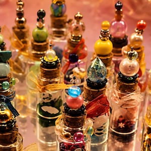 May include: A collection of small glass bottles with cork stoppers, each topped with decorative beads, crystals, and charms in various colours including blue, pink, yellow, and green. The bottles contain small items and are arranged together.