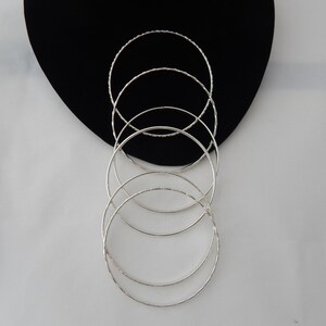 May include: Set of five silver bangles, stacked on top of each other, with a textured finish.