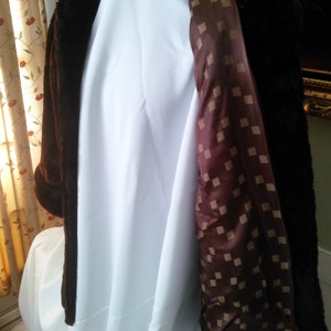 May include: A brown faux fur coat with a brown and white checkered lining. The coat is hanging on a white hanger.