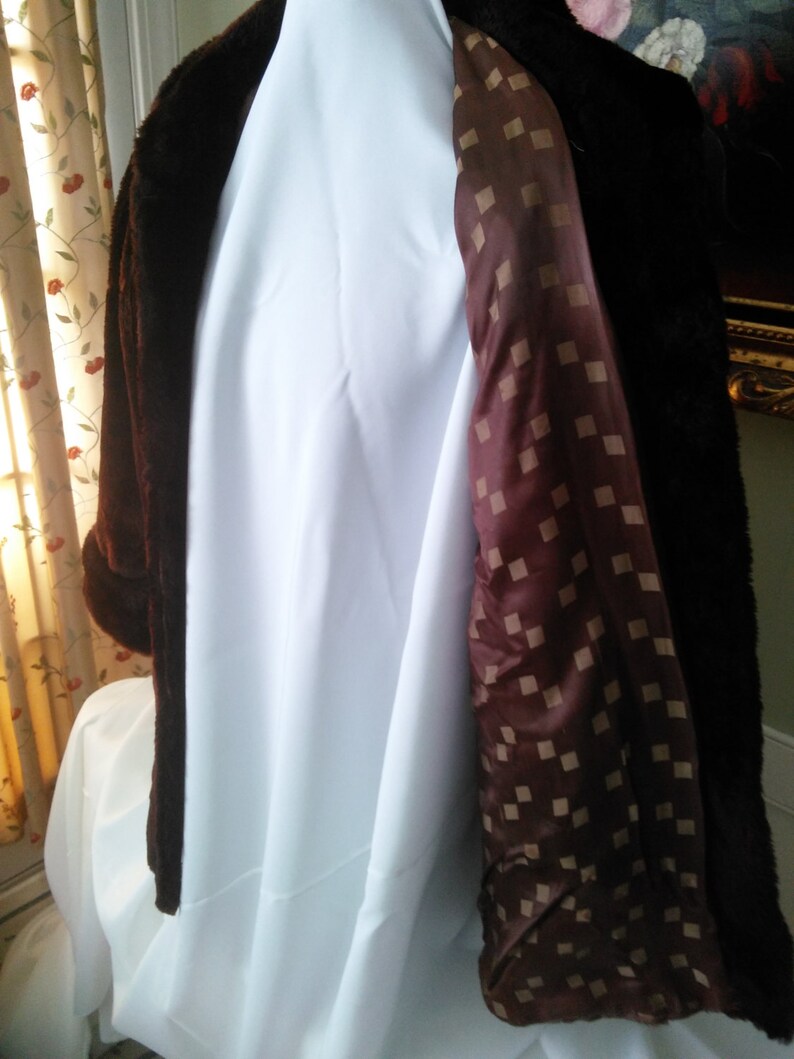 May include: A brown faux fur coat with a brown and white checkered lining. The coat is hanging on a white hanger.