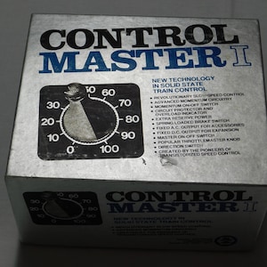May include: A silver rectangular box for a Control Master I train controller. The top features a black dial graphic numbered 0 to 100 and text listing features like solid state train control, momentum circuitry, and a spring loaded brake switch.