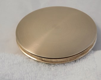 May include: A round, gold-colored metal lid with a smooth, brushed finish. The lid has a slightly raised edge.