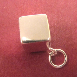 May include: A silver charm in the shape of a cube with a round loop attached. The charm is smooth and shiny.