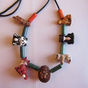 May include: A necklace with a black cord and colorful beads featuring animal figurines. The beads include a panda, a fox, a hedgehog, a koala, a cat, and a lion.