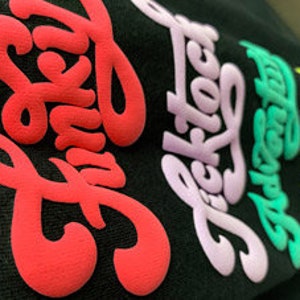 May include: A black t-shirt with five different colored words printed on it. The words are "Funky", "Ticktock", "Adventure", "Free", and "Love".
