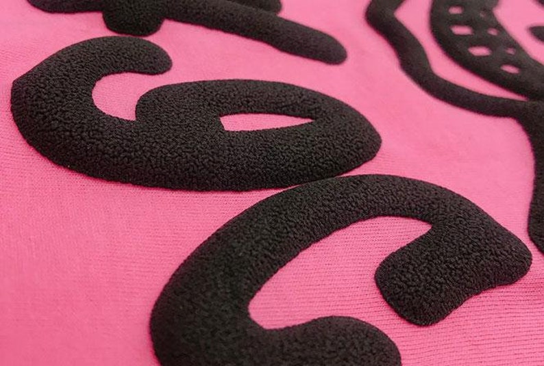 May include: Close-up of a pink fabric with black raised lettering that reads "Coco".