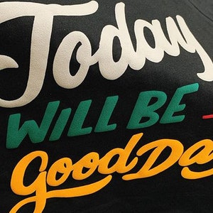 May include: A black t-shirt with the text "Today will be a good day" in white, green, orange, and red lettering.