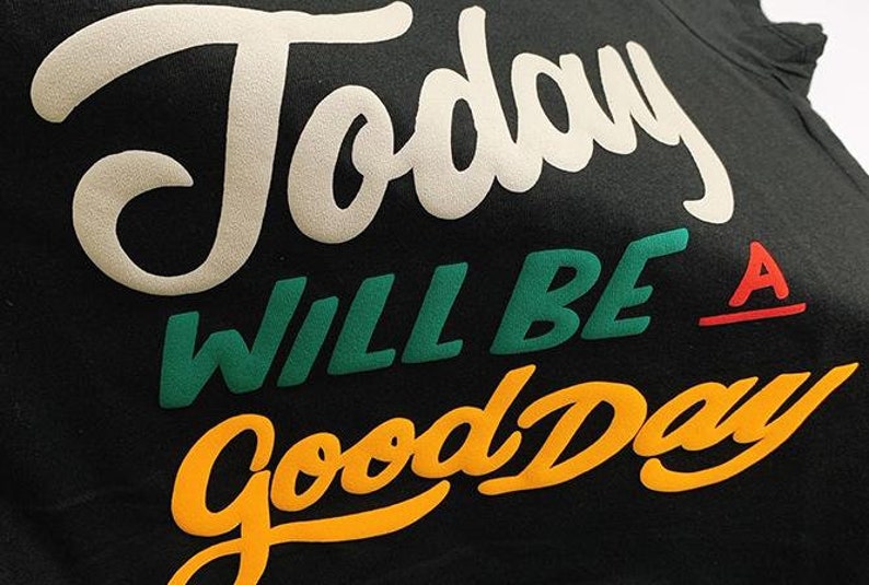 May include: A black t-shirt with the text "Today will be a good day" in white, green, orange, and red lettering.