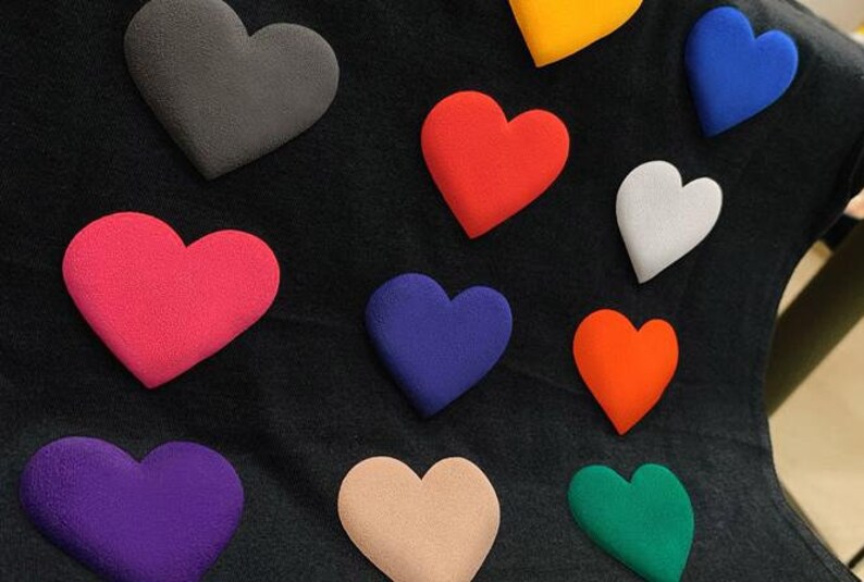 May include: A black fabric background with ten colorful felt hearts in various shades of red, pink, purple, blue, green, orange, yellow, and gray.