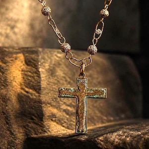 May include: A bronze-toned metal necklace featuring a chain with alternating textured spherical beads and small floral-shaped links. The pendant is a crucifix with a weathered patina finish, depicting a figure and the letters INRI at the top.