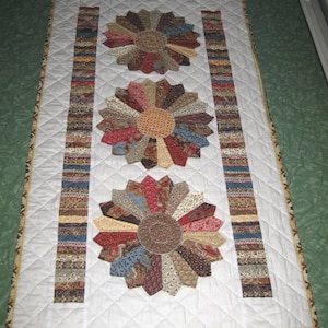 May include: A white quilt with three brown, red and blue pinwheel designs. The quilt has a white background and a brown, red and blue border.