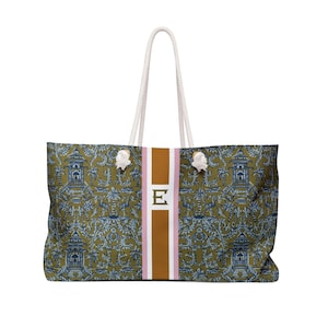 May include: Large tote bag with a repeating pattern of blue pagodas and foliage on an olive green background. The bag features a vertical stripe with the letter "E" in the center, and white rope handles.