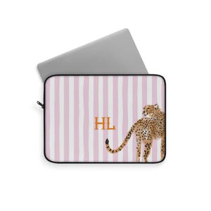 May include: Laptop sleeve with a pink and white striped pattern. The sleeve features the initials "HL" in orange and a cheetah illustration on the right side. The laptop sleeve is black around the edges.