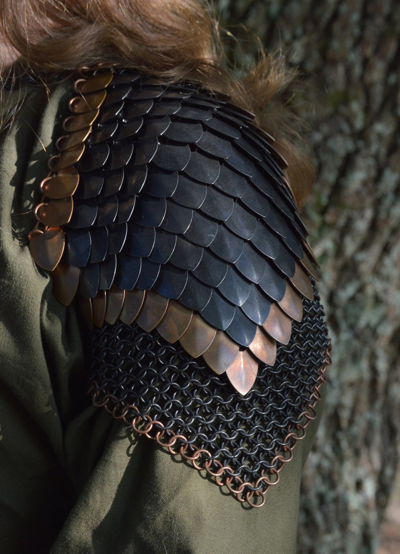 May include: Black and copper chainmail shoulder armor with a scale design. The armor is made of metal rings and scales.
