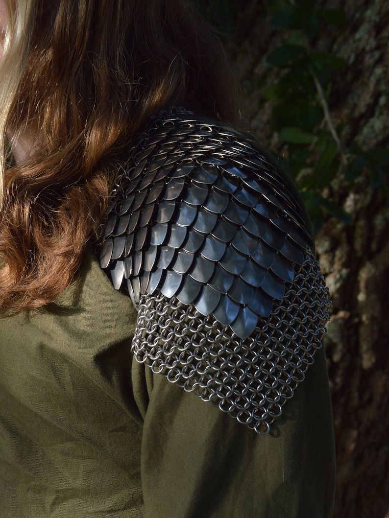 May include: A silver chainmail shoulder armor with a scale design. The armor is worn over a green shirt.