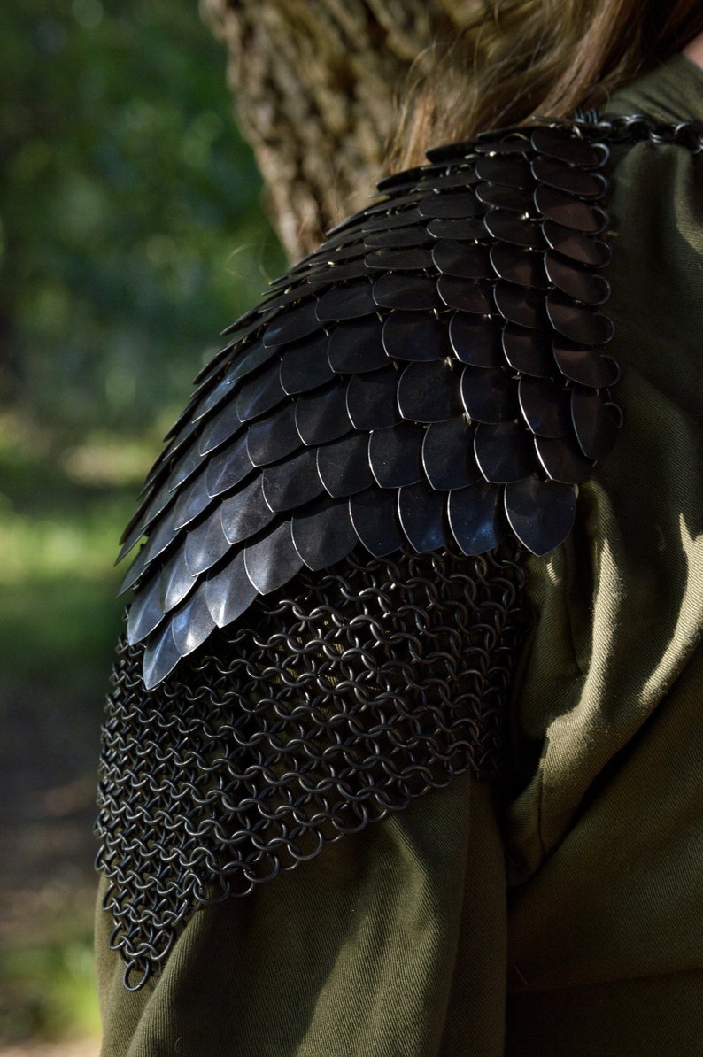 May include: Black chainmail shoulder armor with a black scalemail overlay. The armor is worn over a green garment.