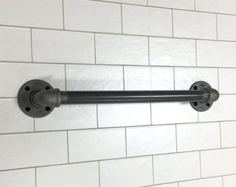 May include: A black industrial-style towel bar made of metal pipes, mounted on a white tiled wall. The bar features a straight horizontal pipe connected to circular flanges on each end, creating a sturdy and functional design.