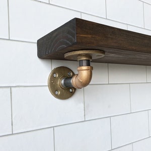 May include: A dark brown wooden shelf with a gold metal pipe bracket. The bracket has a round flange and a pipe that is bent at a 90-degree angle.