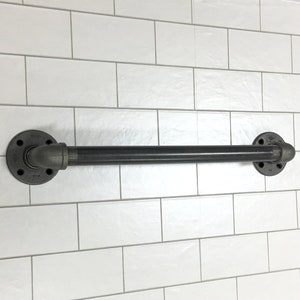 May include: Black industrial pipe towel bar mounted on a white tiled wall. The bar is approximately 24 inches long.